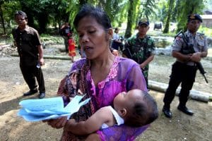 A resident holds her baby as she prays during attend Sunday mass as a soldier and policemen stand guard near a burned church at Suka Makmur Village in Aceh Singkil